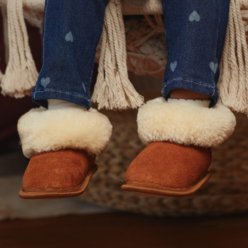 Child's legs wearing blue jeans and camel sheepskin toddler slippers with white fur.
