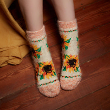 Woman's legs in home interior wearing goat wool white orange socks with sunflower design.