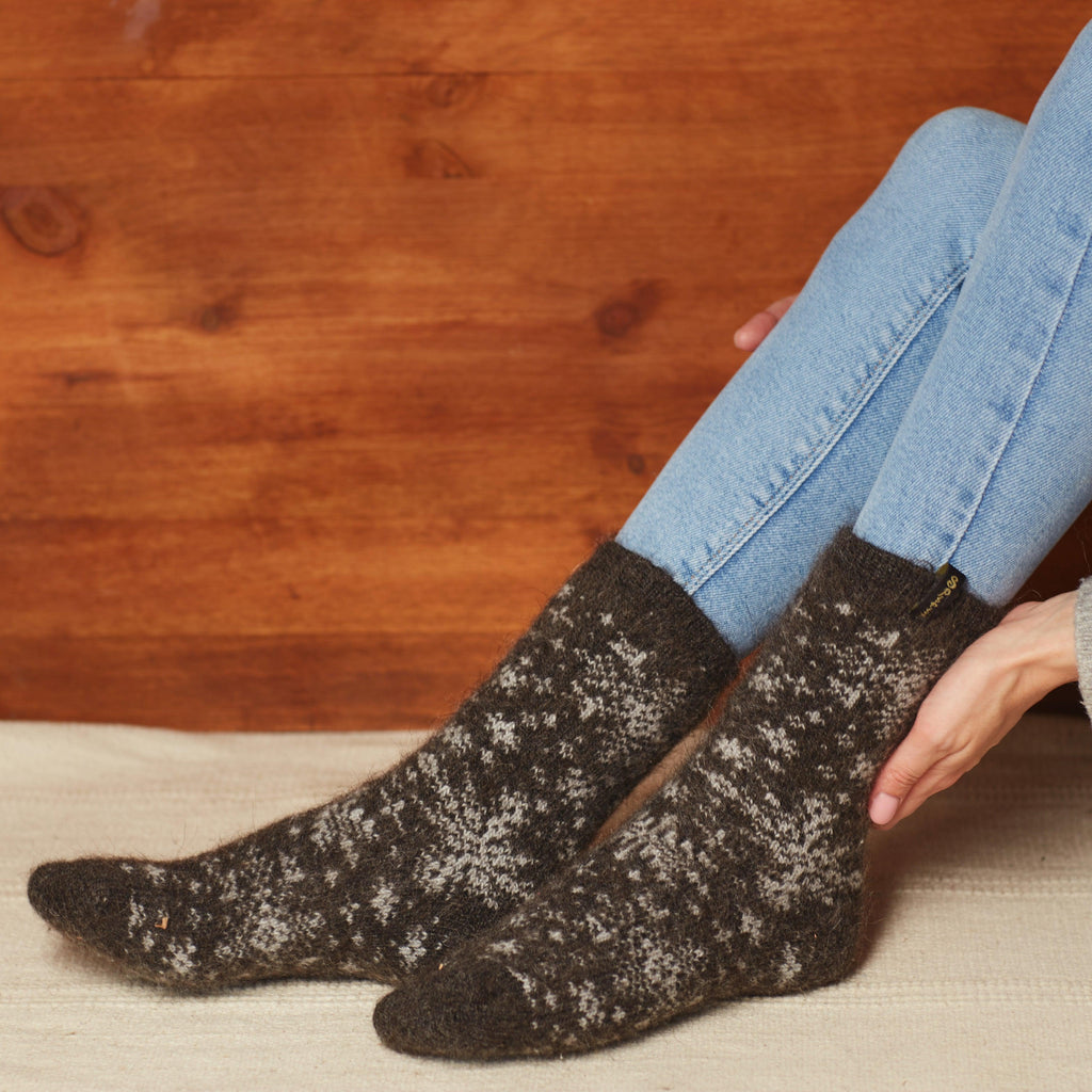 Woman's legs in home settings wearing jeans and black goat hair thick socks with white snowflakes.