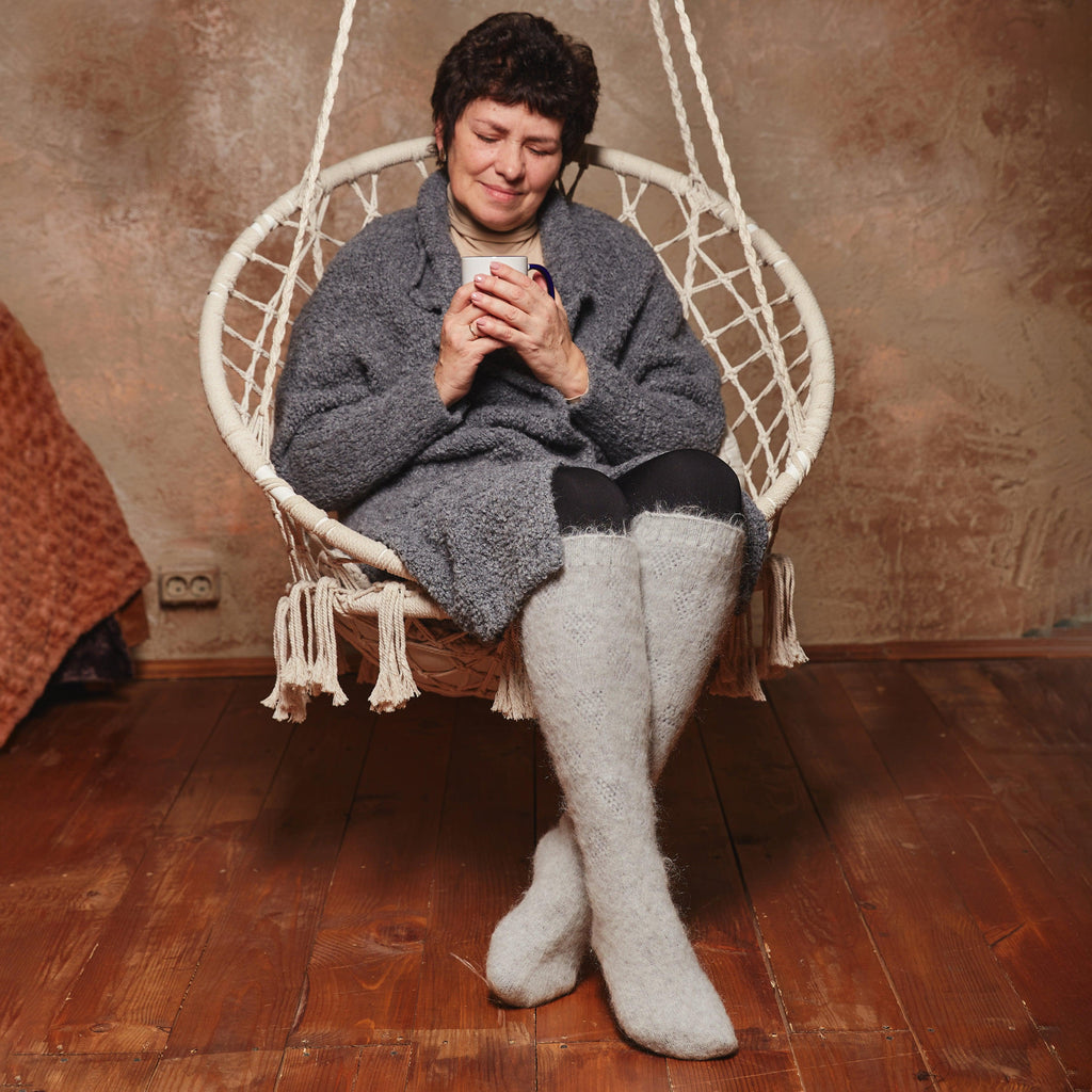 Woman sitting in a hanging chair wearing gray goat wool knee-high socks.
