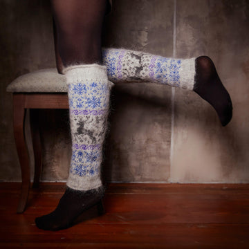 Woman's legs in home interior wearing grey goat hair leg warmers with deer and snowflake design.